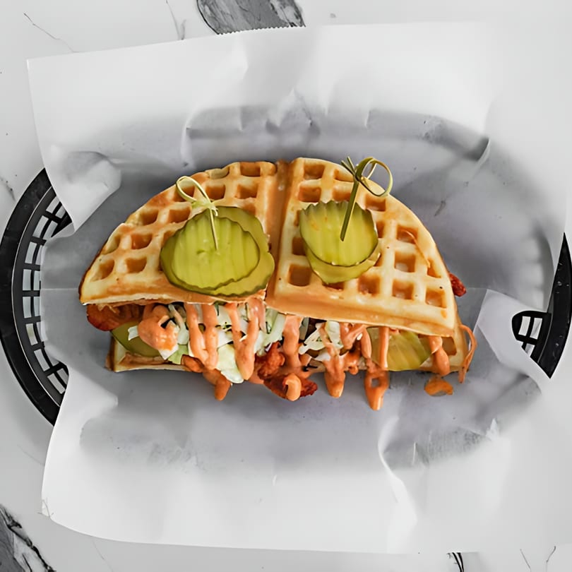 Sumah Hot Chicken's waffle sandwich with fried chicken, coleslaw, sauce, and pickles in a basket.