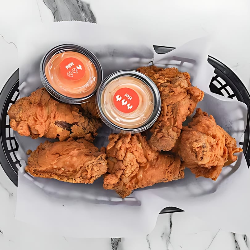 Sumah Hot Chicken's fried chicken pieces and two dipping sauces in a black basket.