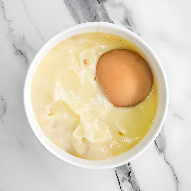 Sumah Hot Chicken's banana pudding dessert with a vanilla wafer, in a white bowl on a marble surface.