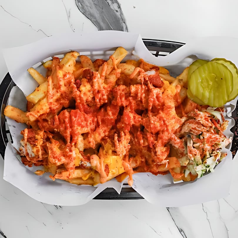 Sumah Hot Chicken's loaded fries with spicy sauce, cheese, coleslaw, and pickles in a basket.